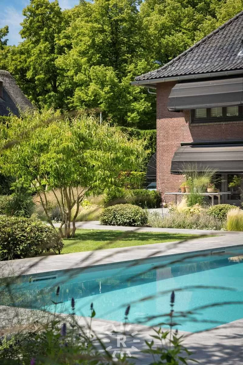 Modern zwembad met turquoise water, strak betegeld terras en weelderige beplanting